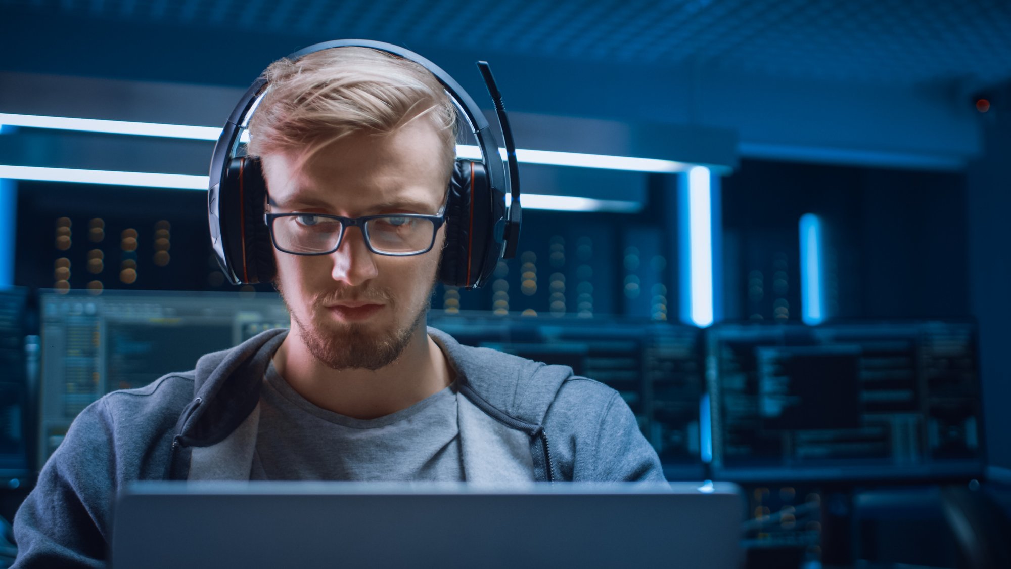 portrait-d-un-developpeur-de-logiciels-un-hacker-un-joueur-portant-des-lunettes-et-un-casque-assis-a-son-bureau-et-travaillant-jouant-sur-un-ordinateur-portable-a-l-arriere-plan-un-environnement-de-haute-technol portrait-d-un-developpeur-de-logiciels-un-hacker-un-joueur-portant-des-lunettes-et-un-casque-assis-a-son-bureau-et-travaillant-jouant-sur-un-ordinateur-portable-a-l-arriere-plan-un-environnement-de-haute-technol